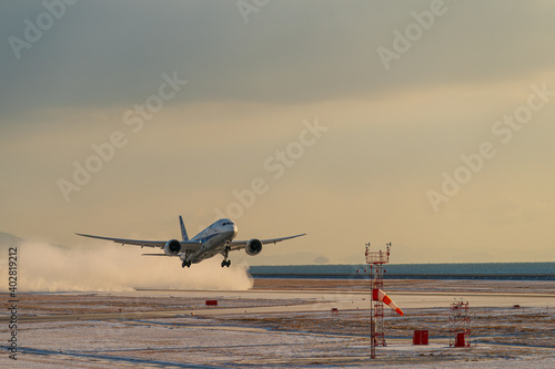 小雪舞う空港を雪煙を上げながら離陸する航空機