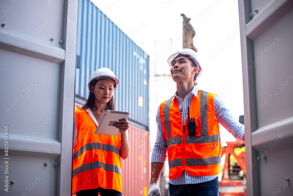 Asian dock control man and woman logistics worker wear safety helmets and protect suite open cargo container door and working and checking product with taplets and scan code gun.. Asian dock control man and woman logistics worker wear safety helmets and protect suite open cargo container door and working and checking product with taplets and scan code gun..