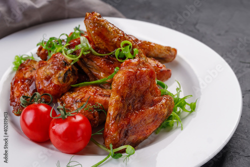 barbecue chicken wings in a white plate on a dark background. Buffalo wings decorated with greens and cherry tomatoes