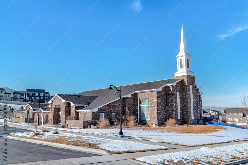 Church exterior view amidst snowy neighborhood against blue sky in winter