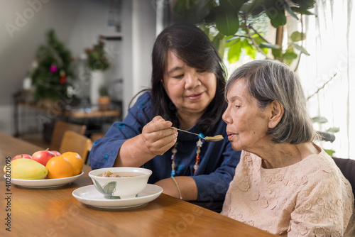 Daughter feeding elderly mother with soup. photo
