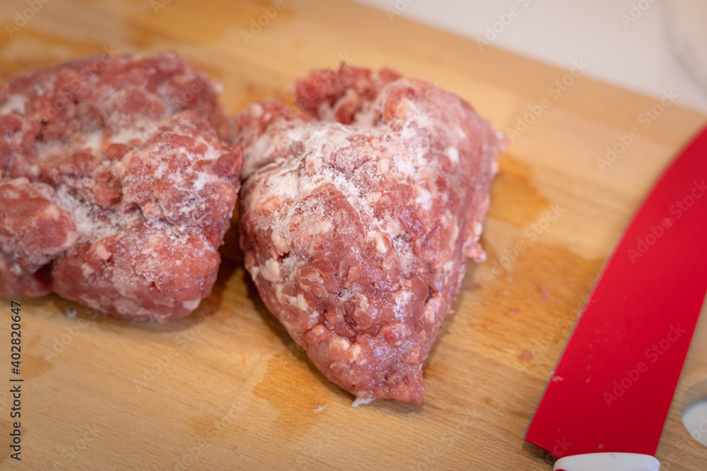 A piece of frozen chopped pork meat on the wooden cutting board, prepare for cooking in the kitchen. Food close-up and selective focus photo. A piece of frozen chopped pork meat on the wooden cutting board, prepare for cooking in the kitchen. Food close-up and selective focus photo.