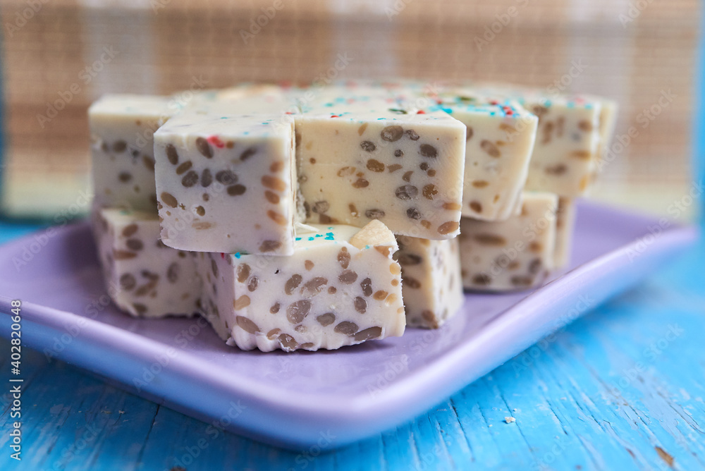 Samarkand halva cut into rhombuses with pistachios and cashews and blue and red pastry topping on a purple rectangular plate. Selective focus. Close up Samarkand halva cut into rhombuses with pistachios and cashews and blue and red pastry topping on a purple rectangular plate. Selective focus. Close up