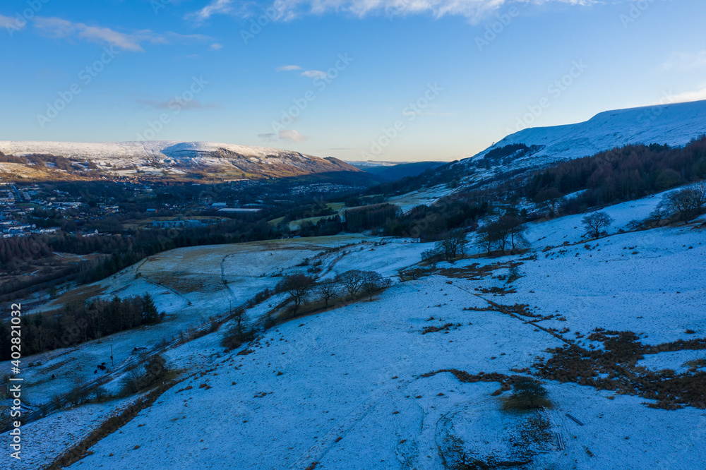 Aerial drone view of snow covered mountains and towns rising above the south east valleys, Wales