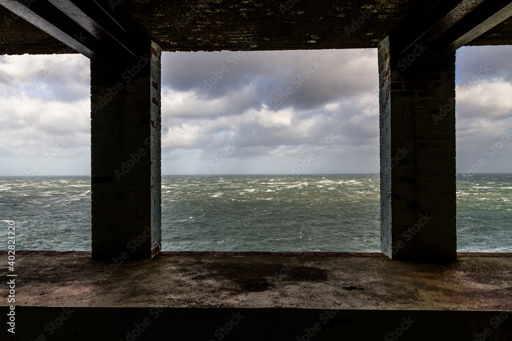 Lookout in derelict building looking out to stormy sea with two pillars.