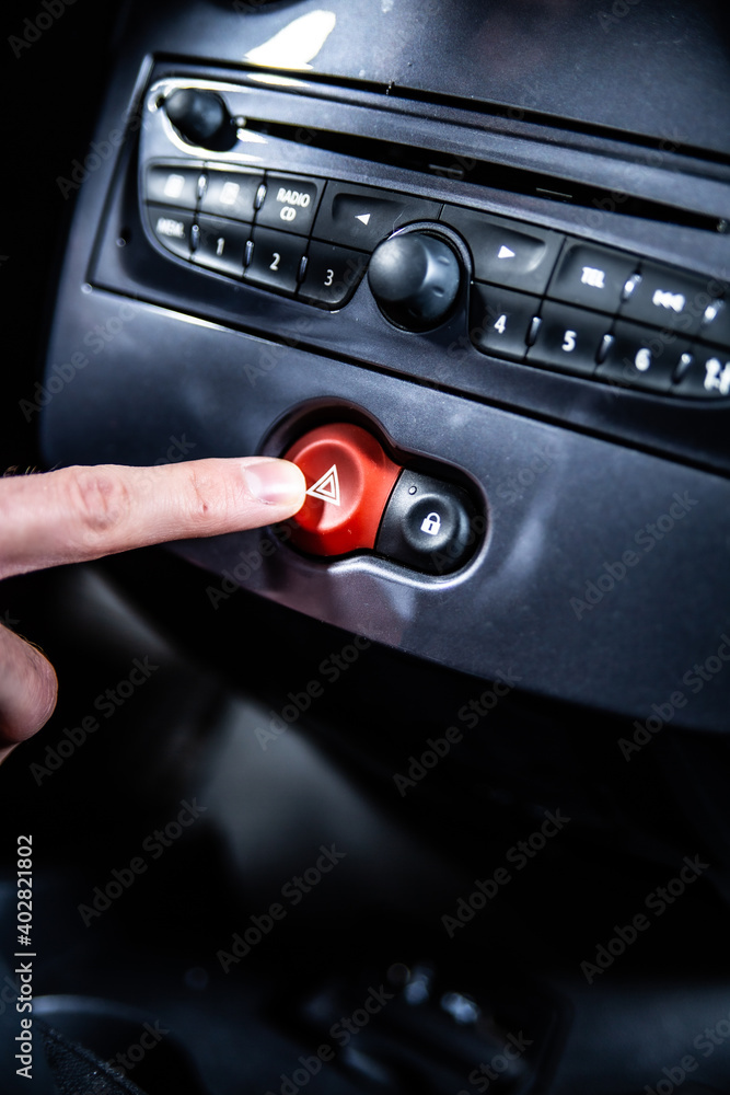 Fototapeta premium Pressing a hazard warning lights button on a car dashboard.