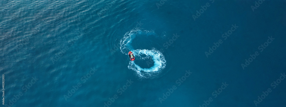 Aerial drone ultra wide photo of jet ski watercraft performing extreme manoeuvres in deep blue bay with calm sea at dusk Aerial drone ultra wide photo of jet ski watercraft performing extreme manoeuvres in deep blue bay with calm sea at dusk