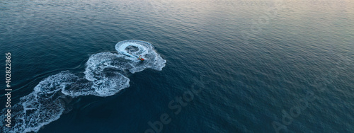 Aerial drone ultra wide photo of jet ski watercraft performing extreme manoeuvres in deep blue bay with calm sea at dusk