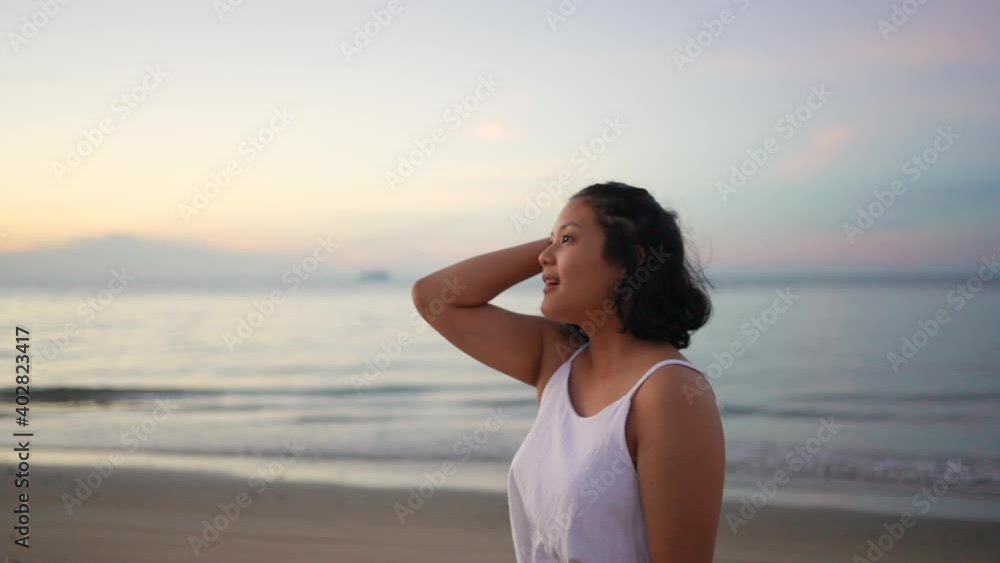 Happy beautiful Asian woman in white dress walking on tropical island beach on island beach in summertime at sunrise. Smiling woman relax and enjoy outdoor lifestyle in summer holiday vacation. Happy beautiful Asian woman in white dress walking on tropical island beach on island beach in summertime at sunrise. Smiling woman relax and enjoy outdoor lifestyle in summer holiday vacation.