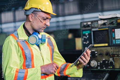 engineer / worker man caucasian in protective safety jumpsuit uniform with yellow hardhat and using digital tablet at factory.Metalworking industry concept professional engineer manufacturing machine