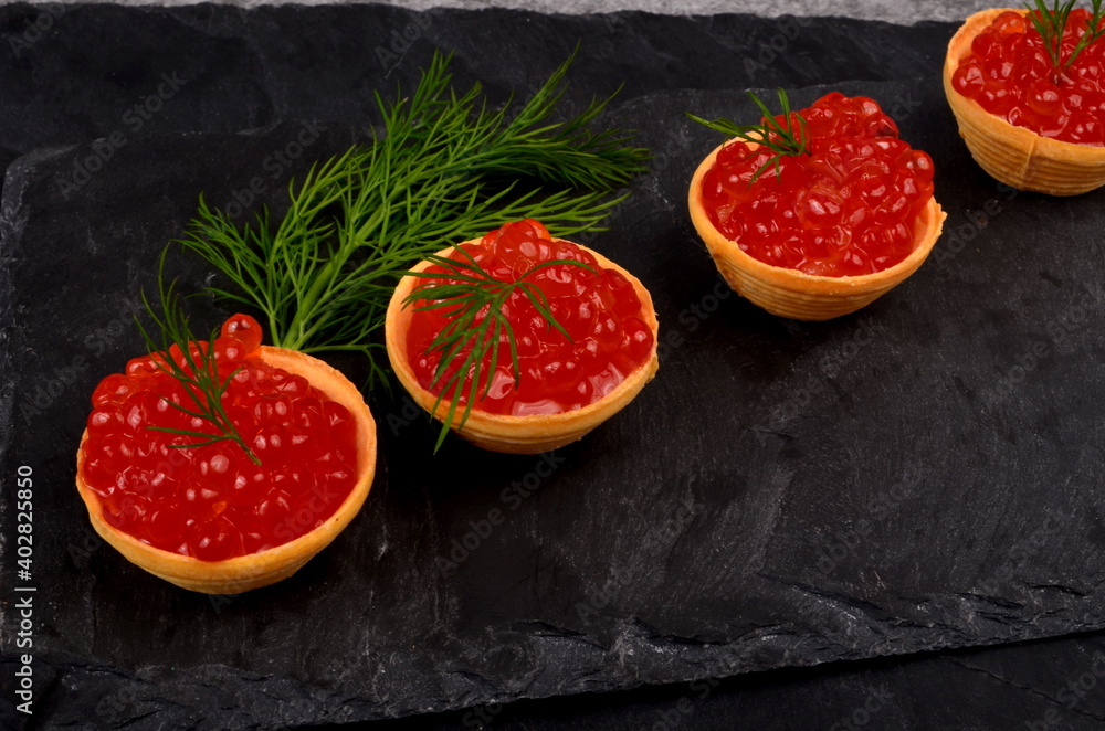 Tartlets with red salmon caviar on black stone plate, decorated with green dill, close - up. Copy space. Seafood appetizer Tartlets with red salmon caviar on black stone plate, decorated with green dill, close - up. Copy space. Seafood appetizer