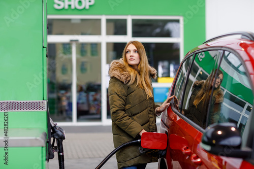 Young caucasian woman at self-service gas station, hold fuel nozzle and refuel the car with petrol, diesel, gas. Pretty woman filling her auto with gasoline or benzine, outdoors. Self service gas pump photo