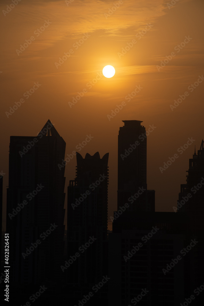 Dubai skyline at sunset with orange and yellow sky over the skyscrapers in the United Arab Emirates. (Portrait View)