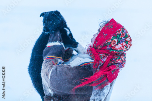 A young girl, in the national winter clothes of the northern inhabitants of the tundra, plays with a dog