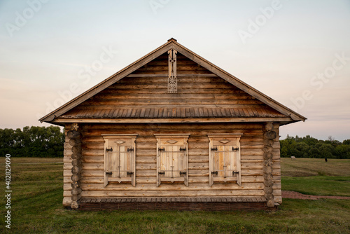 old carved wooden house on a green meadow, front view