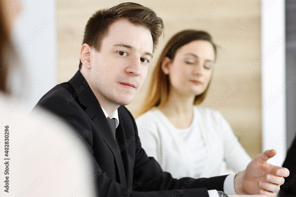 Businessman headshot at meeting in modern office. Unknown entrepreneur sitting with colleagues at the background. Teamwork and partnership concept Businessman headshot at meeting in modern office. Unknown entrepreneur sitting with colleagues at the background. Teamwork and partnership concept