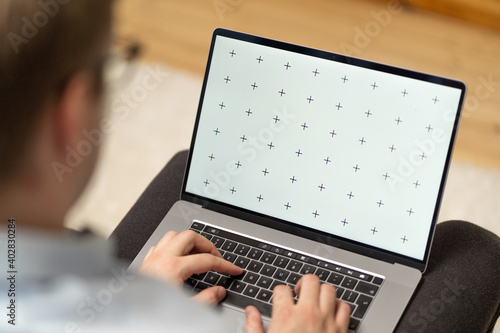 Man with glasses holds laptop in lap, browsing internet or application with blank screen mock-up for your design at home office with blurry background with free space for custom text about business