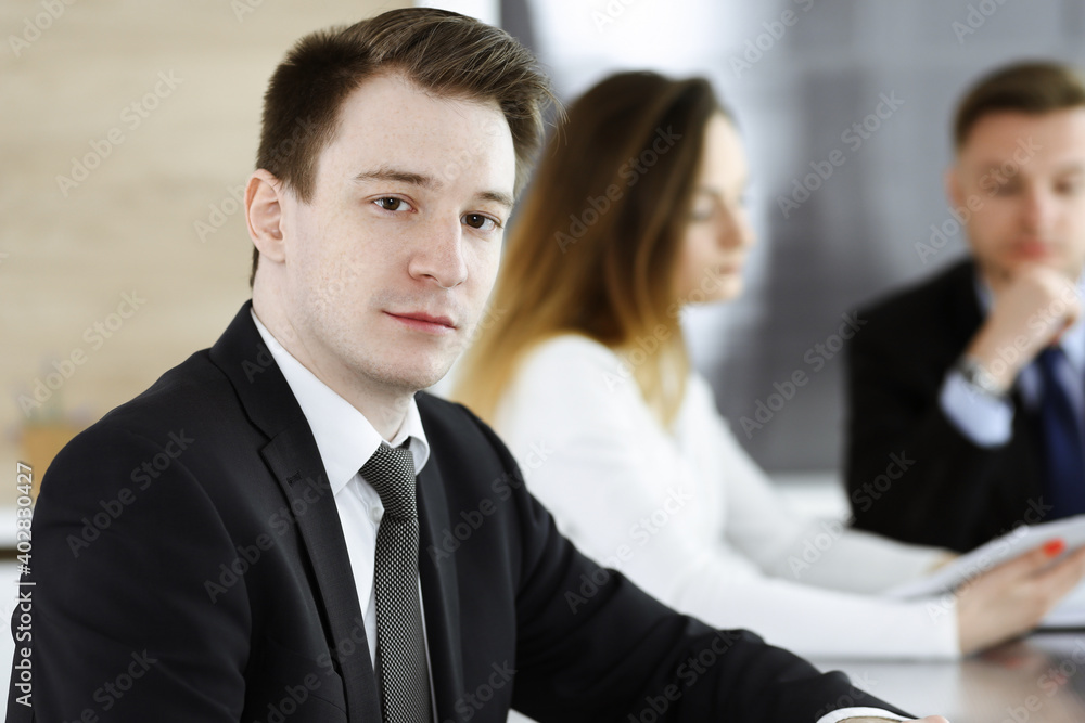 Businessman headshot at meeting in modern office. Unknown entrepreneur sitting with colleagues at the background. Teamwork and partnership concept Businessman headshot at meeting in modern office. Unknown entrepreneur sitting with colleagues at the background. Teamwork and partnership concept