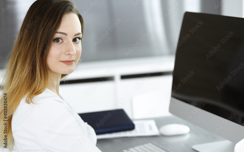 Business woman headshot at workplace in modern office. Unknown businesswoman sitting behind computer monitor. Young accountant or secretary looks good Business woman headshot at workplace in modern office. Unknown businesswoman sitting behind computer monitor. Young accountant or secretary looks good