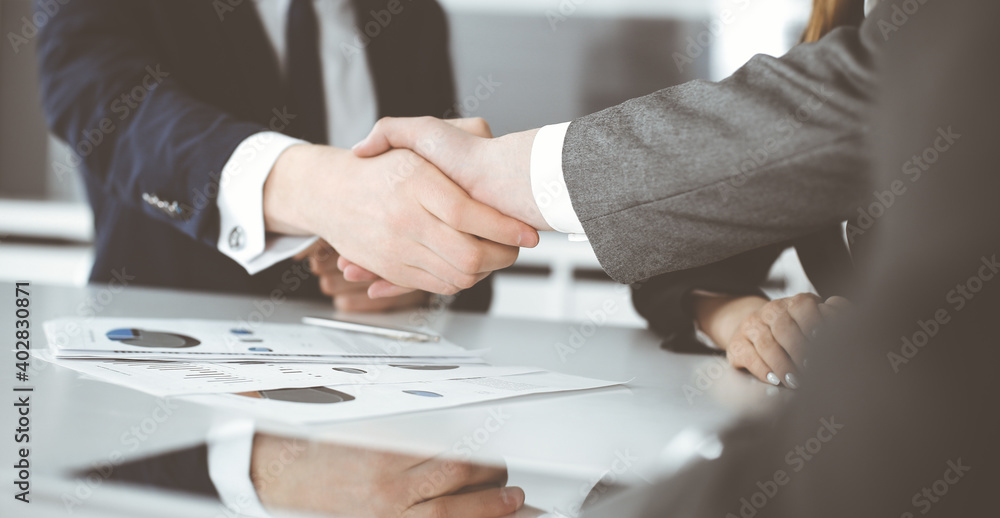 Unknown businessman shaking hands with his colleague or partner above the glass desk in modern office, close-up. Business people group at meeting Unknown businessman shaking hands with his colleague or partner above the glass desk in modern office, close-up. Business people group at meeting