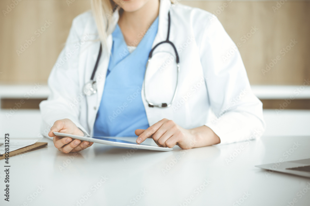 Unknown woman-doctor standing in clinic and using tablet pc, close-up. Data and best service in medicine and healthcare Unknown woman-doctor standing in clinic and using tablet pc, close-up. Data and best service in medicine and healthcare