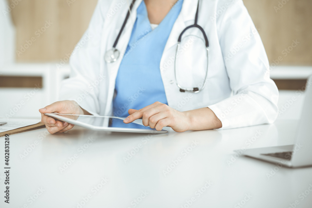 Unknown woman-doctor standing in clinic and using tablet pc, close-up. Data and best service in medicine and healthcare Unknown woman-doctor standing in clinic and using tablet pc, close-up. Data and best service in medicine and healthcare