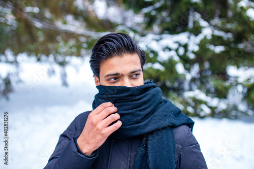 indian man enjoying snowflakes falling from upwards in forest wrapped nose and mouth with the scarf becouse he he forgot the medical mask photo