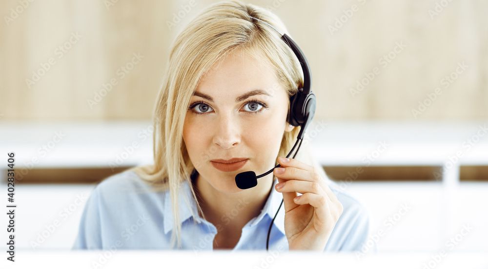 Blonde business woman sitting and communicated by headset in call center office. Concept of telesales business or home office occupation Blonde business woman sitting and communicated by headset in call center office. Concept of telesales business or home office occupation