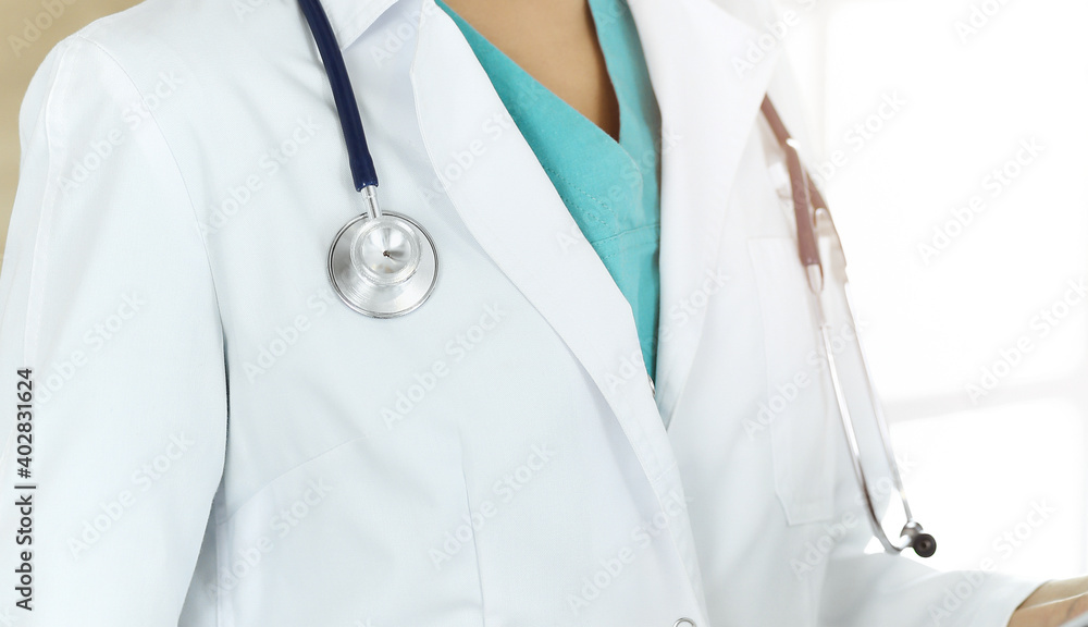 Unknown female doctor standing with stethoscope in sunny clinic, close-up Unknown female doctor standing with stethoscope in sunny clinic, close-up