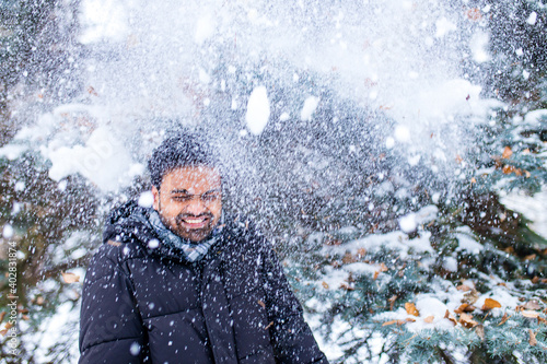 indian man enjoying snowflakes falling from upwards in forest