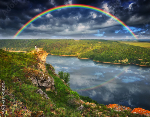 rainbow over the river. woman on a cliff above the canyon 