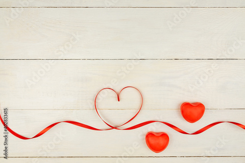 Creative Valentine Day romantic composition with red hearts, satin ribbon on wooden background. Mockup with copy space for blogs and social media.