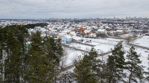 A view from a height of a small snow-covered village against the backdrop of a city and forest