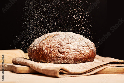 Fresh made bread on a cloth napkin with flour falling from top. Roller and chopping board visible in the background. Natural homemade ingredients. Dark background, brown color grading.