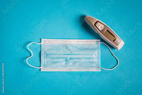Medical face mask and thermometer on blue background. Covid protection. © Pablo Rasero