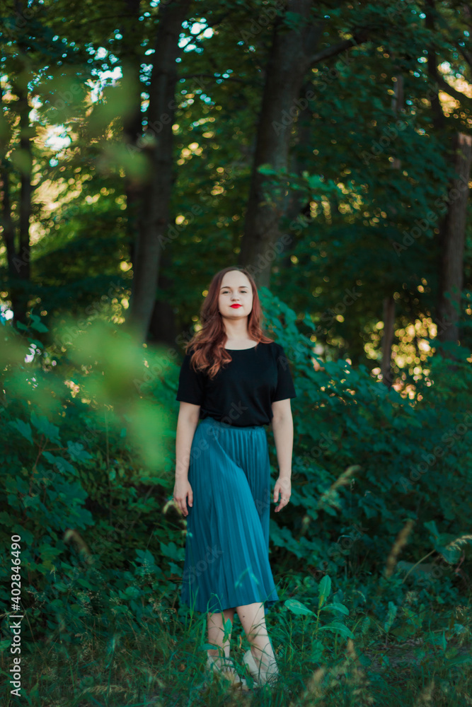 Girl in a turquoise skirt in a fairy forest. Smiling cute girl with red lipstick. Girl on the background of large tree branches Girl in a turquoise skirt in a fairy forest. Smiling cute girl with red lipstick. Girl on the background of large tree branches