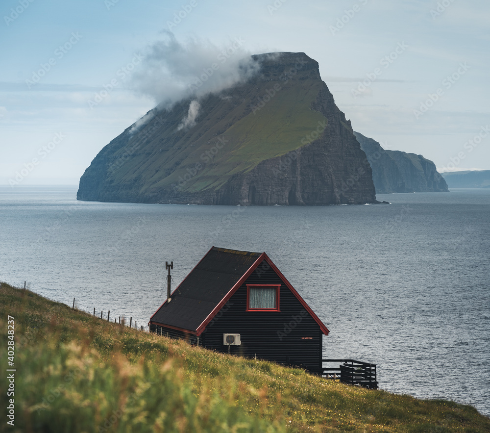 Black house on famous faroese Witches Finger Trail and Koltur island on background. Sandavagur village, Vagar island, Faroe islands, Denmark. Landscape photography