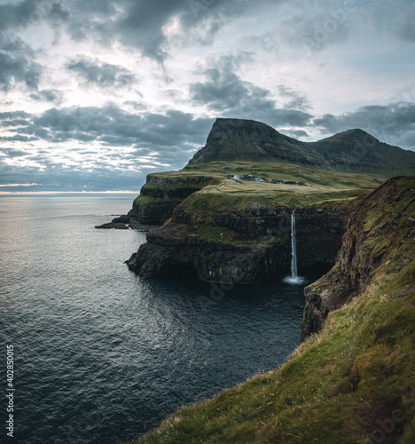 Gasadalur village and Mulafossur its iconic waterfall during sunset in summer with bluw sky. Vagar, Faroe Islands, Denmark. Rough see in the north atlantic ocean.