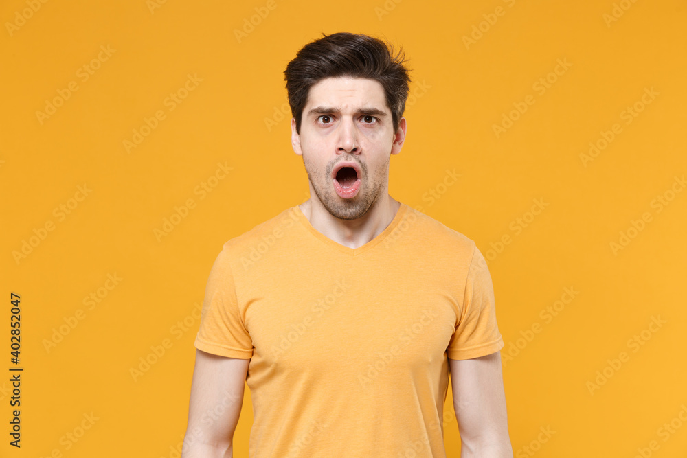 Young shocked confused unshaved caucasian impressed man 20s years old wearing casual basic blank print design t-shirt look camera with open mouth isolated on yellow color background studio portrait Young shocked confused unshaved caucasian impressed man 20s years old wearing casual basic blank print design t-shirt look camera with open mouth isolated on yellow color background studio portrait