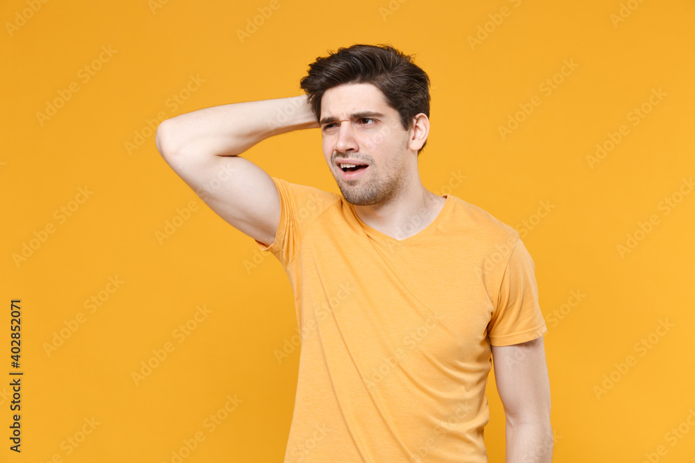 Young confused pensive thoughtful unshaved caucasian handsome man 20s in casual blank print design t-shirt looking aside with raised up hand touch head isolated on yellow background studio portrait. Young confused pensive thoughtful unshaved caucasian handsome man 20s in casual blank print design t-shirt looking aside with raised up hand touch head isolated on yellow background studio portrait.
