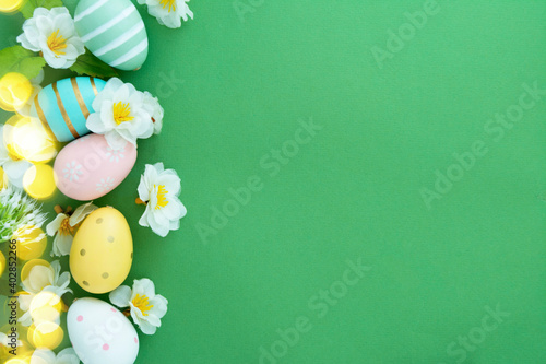 Easter eggs and flowers on green background flat lay with copy space