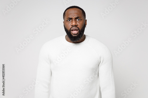 Concerned worried shocked dissatisfied young african american man 20s wearing casual basic sweater standing keeping mouth open looking camera isolated on white color wall background studio portrait.