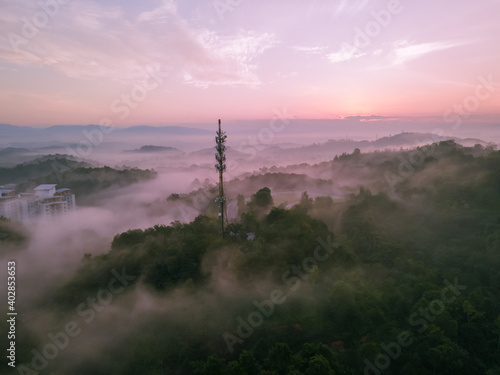 Aerial view of 5G Communication tower during morning sunrise with clouds, mists and fog
