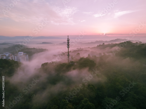Aerial view of 5G Communication tower during morning sunrise with clouds, mists and fog