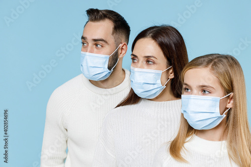 Young parents mom dad with child kid daughter teen girl in sweaters sterile face mask safe from coronavirus virus covid-19 during quarantine isolated on blue background. Family day parenthood concept.