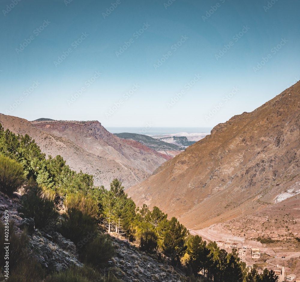 Scenic view of the high atlas mountains directly after sunrise. Wide angle view towards canyon. Berber village in foreground. Trail coming back from the summit of Mount Toubkal, Atlas, Morocco. The