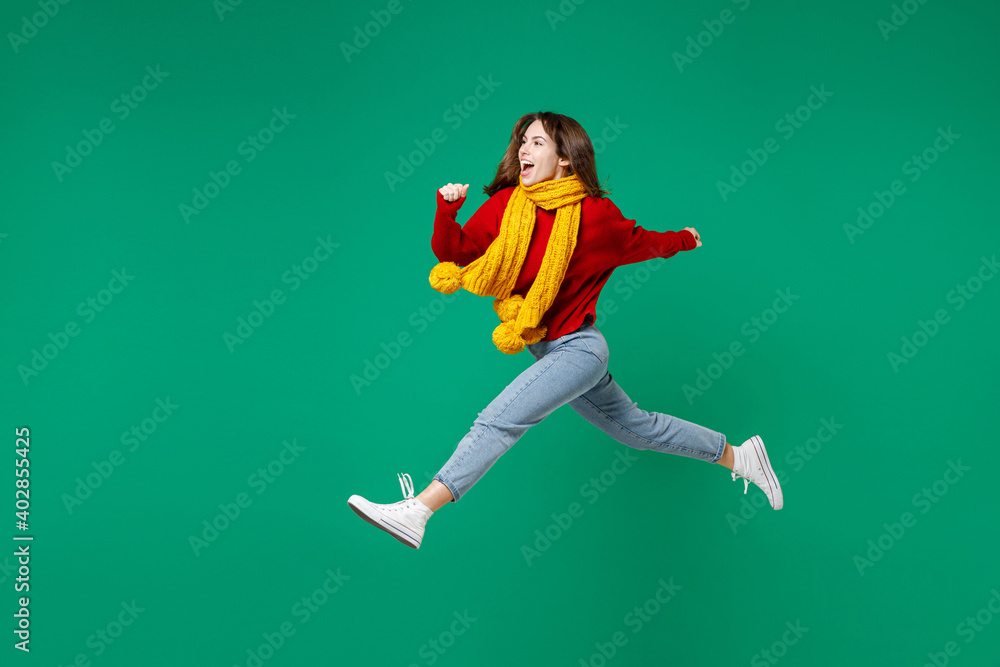 Full length side view of laughing excited young brunette woman 20s wearing basic casual knitted red sweater yellow scarf jumping like running isolated on bright green color background studio portrait. Full length side view of laughing excited young brunette woman 20s wearing basic casual knitted red sweater yellow scarf jumping like running isolated on bright green color background studio portrait.