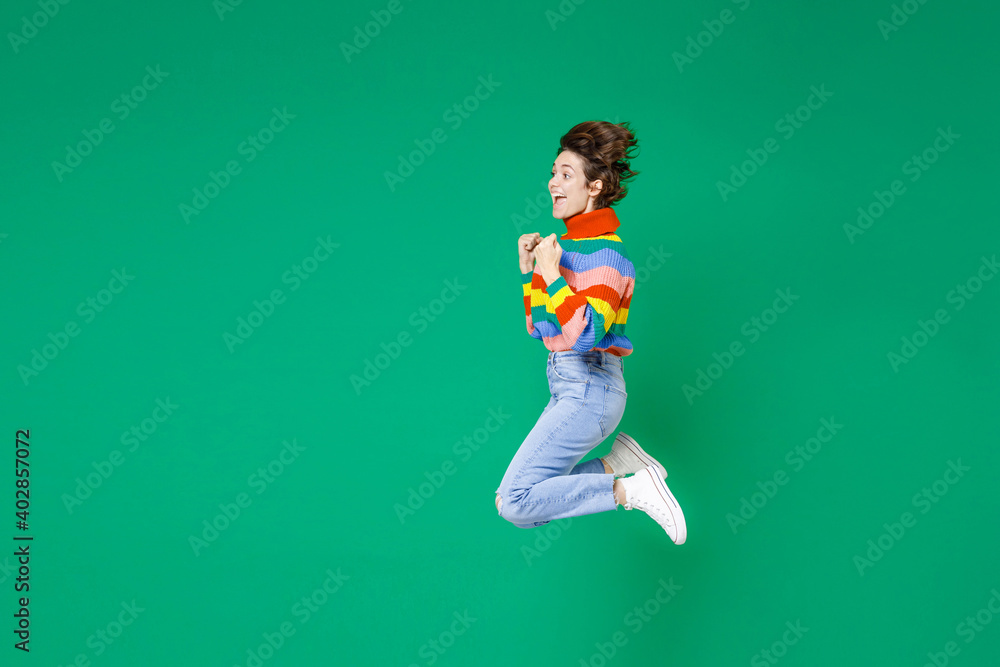Full length side view of excited young brunette woman 20s years old in basic casual colorful sweater jumping doing winner gesture say yes isolated on bright green color background studio portrait. Full length side view of excited young brunette woman 20s years old in basic casual colorful sweater jumping doing winner gesture say yes isolated on bright green color background studio portrait.