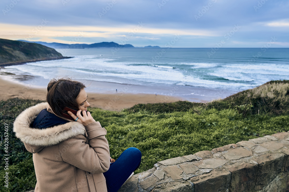 woman talking on the smartphone sitting looking at the views of the sea and the landscape in winter. woman talking on the smartphone sitting looking at the views of the sea and the landscape in winter.