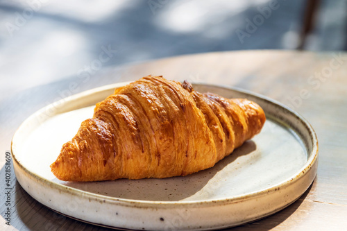 French croissant on plate on wooden table and nature sunlight with shadow through from window.